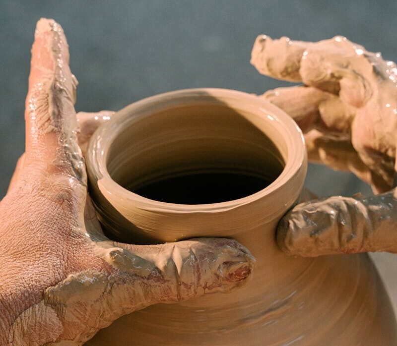 Close-up of hands molding a clay pot, highlighting the art of pottery making.